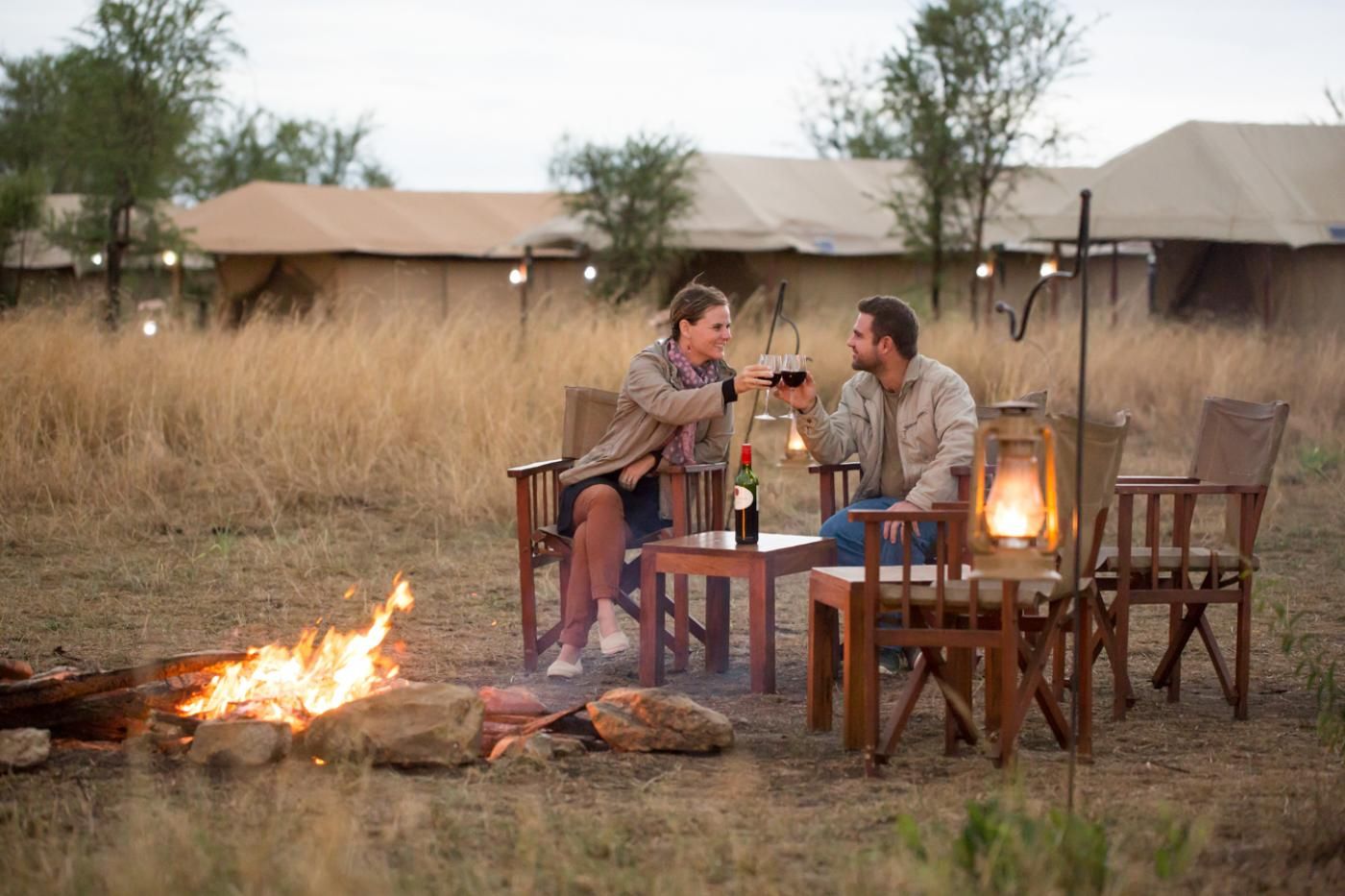 a couple in the evening fire enjoying a drink on their honeymoon safari