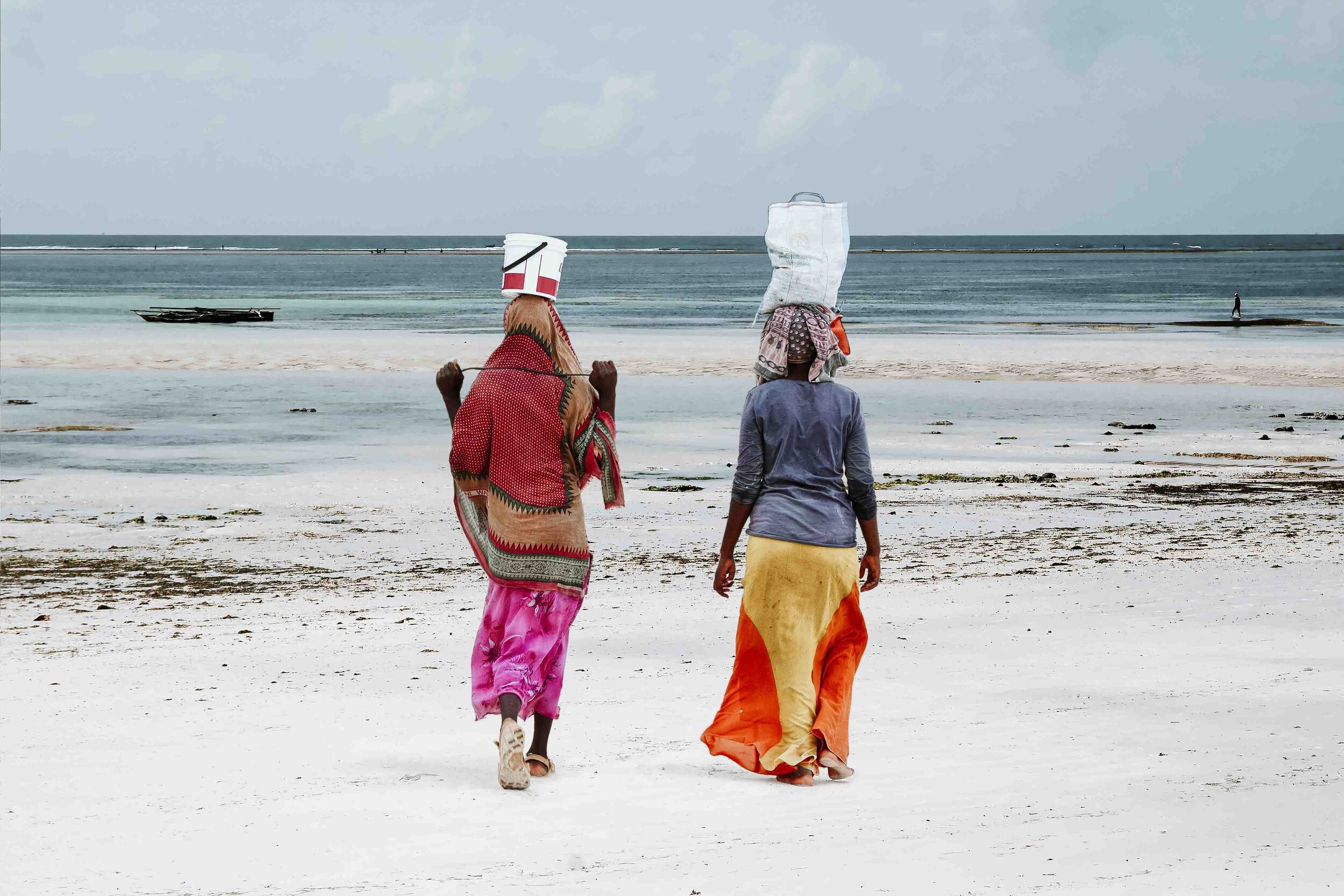 Two Local Women Walking Along the Beach with Something on Their Heads in Local Outfits