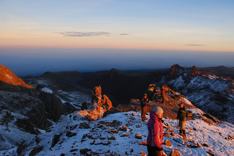 Three climbers standing on Mount Kilimanjaro summit at sunrise, bathed in golden light