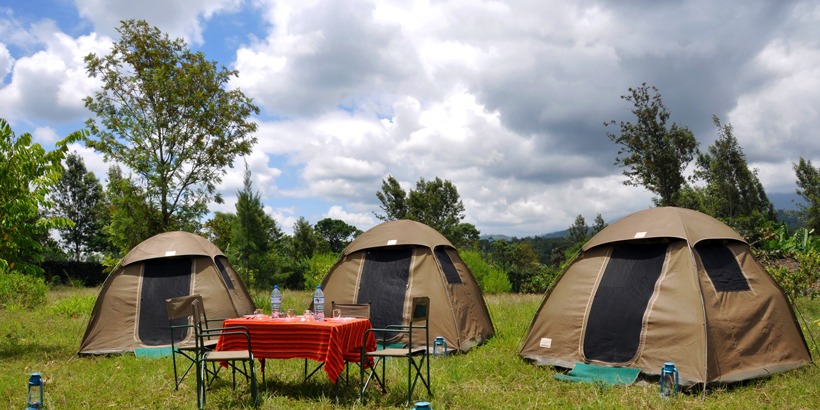 Three safari camping tents with a table and water bottles, set in a peaceful outdoor location.