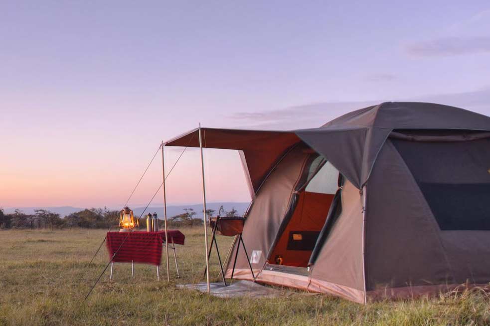 A safari tent illuminated by a lamp at dusk, set against the tranquil Serengeti landscape.