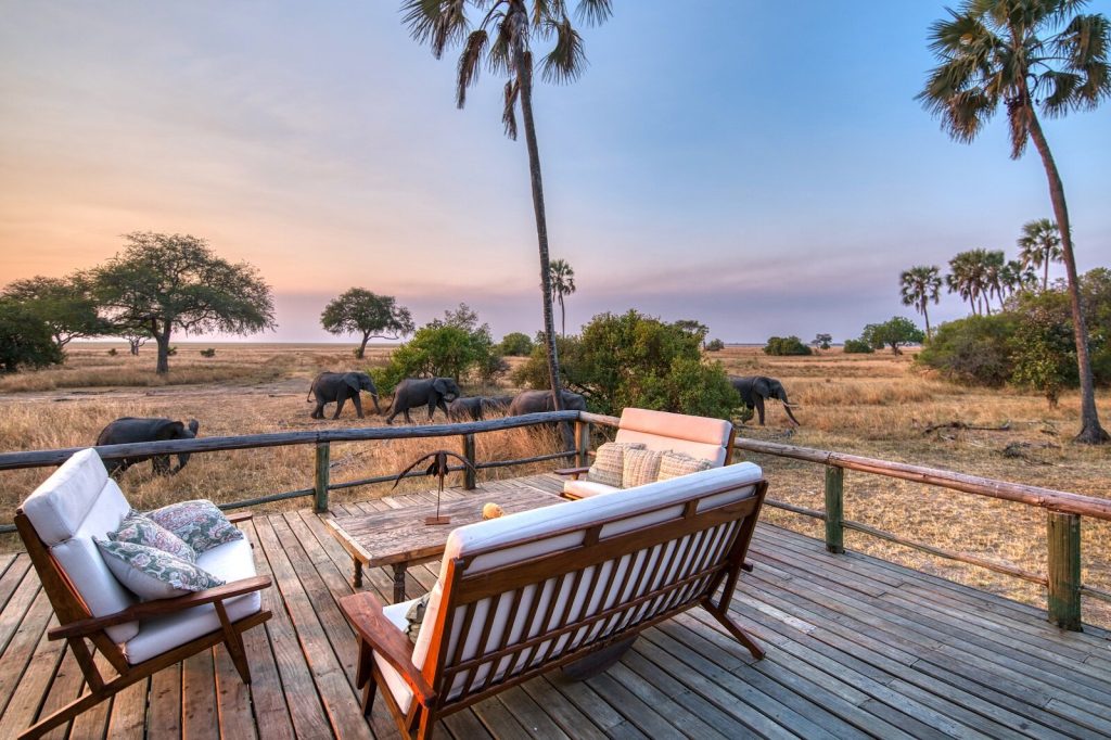 A lodge viewpoint in Katavi National Park with cozy couches and elephants grazing in the background