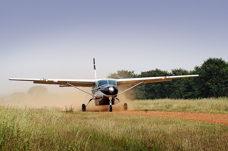 Small plane landing on a dirt airstrip in Serengeti National Park, surrounded by open savannah.