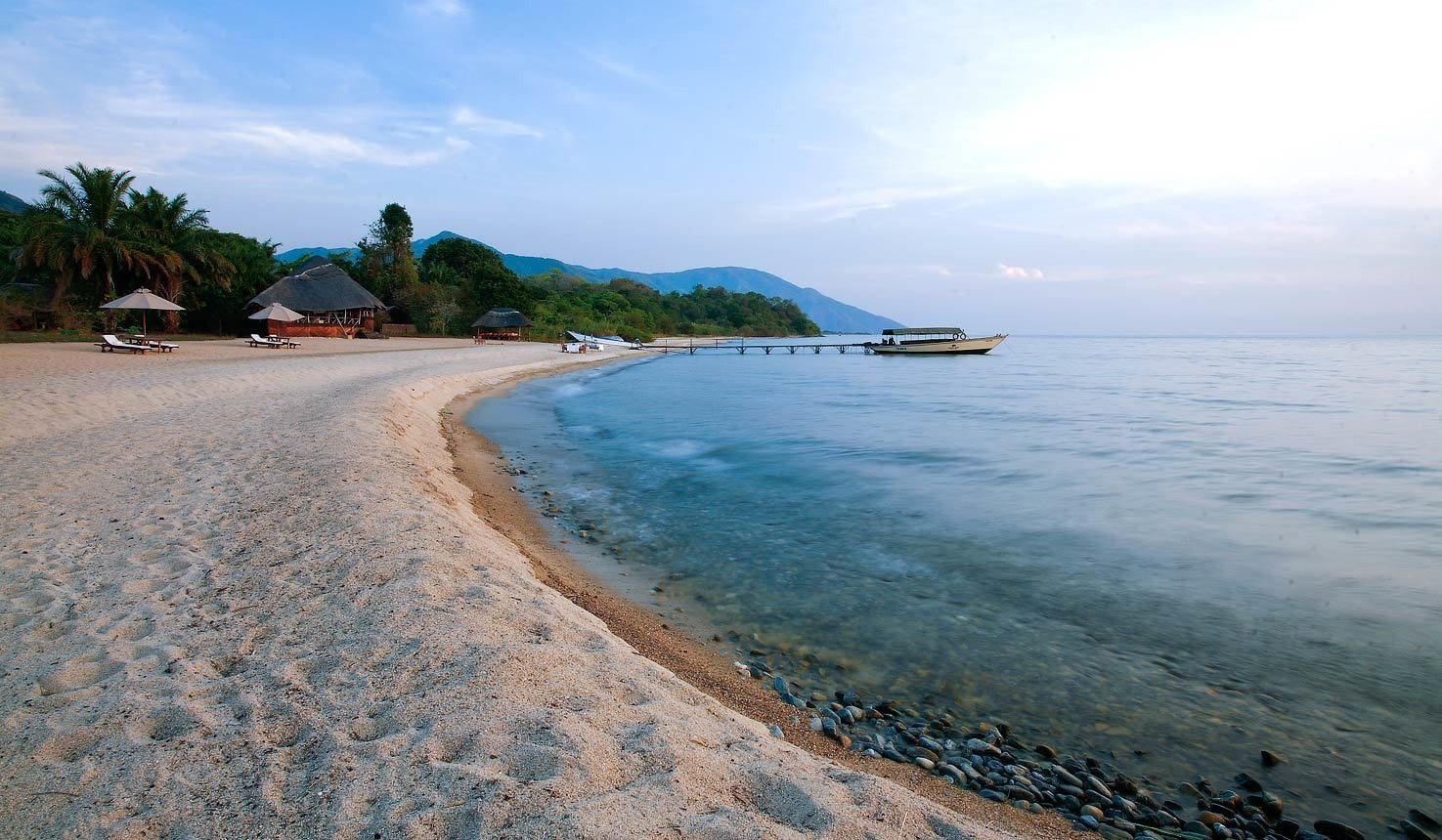 A peaceful beach on Lake Tanganyika with a boat on the water and a safari lodge by the shore, offering a remote and scenic escape in Tanzania.