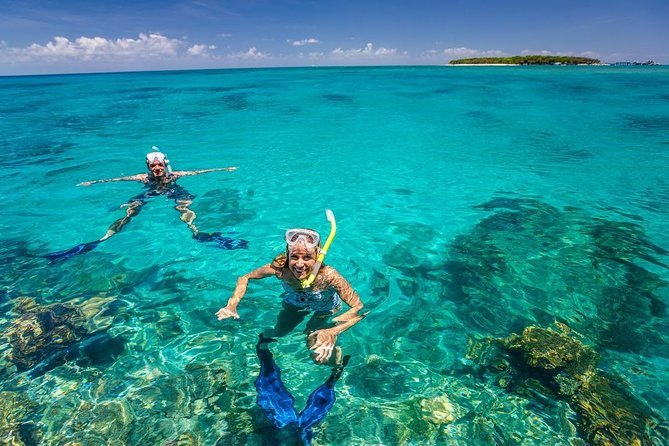 Two tourists snorkeling underwater in Mnemba Atoll, surrounded by colorful coral reefs and tropical fish.