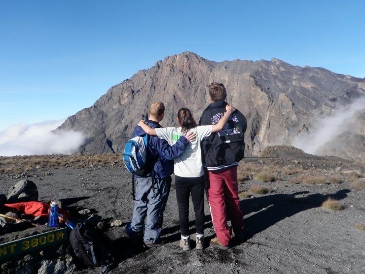 Family standing at the peak of Mount Meru, enjoying panoramic views after a thrilling trek in Tanzania.