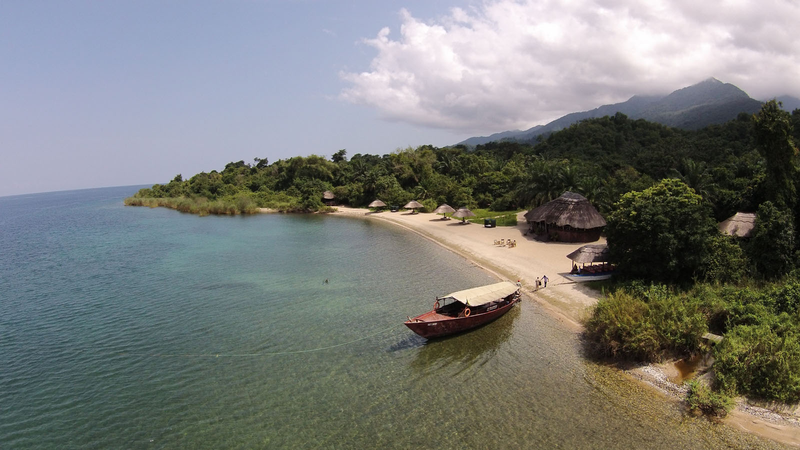 A scenic Lake Tanganyika beach with a boat in the waters and a row of safari lodges lining the shore—an ideal destination for relaxation and adventure in Tanzania