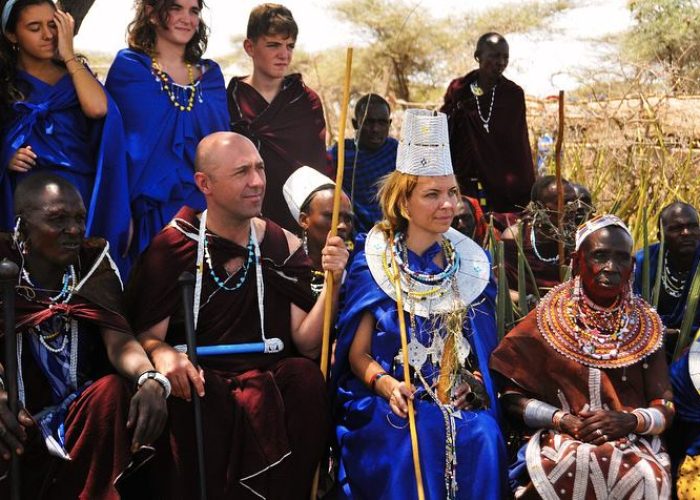 A group of people in Maasai garments seated with local Maasai individuals, with others standing in the background during the Ngorongoro Marathon celebration.